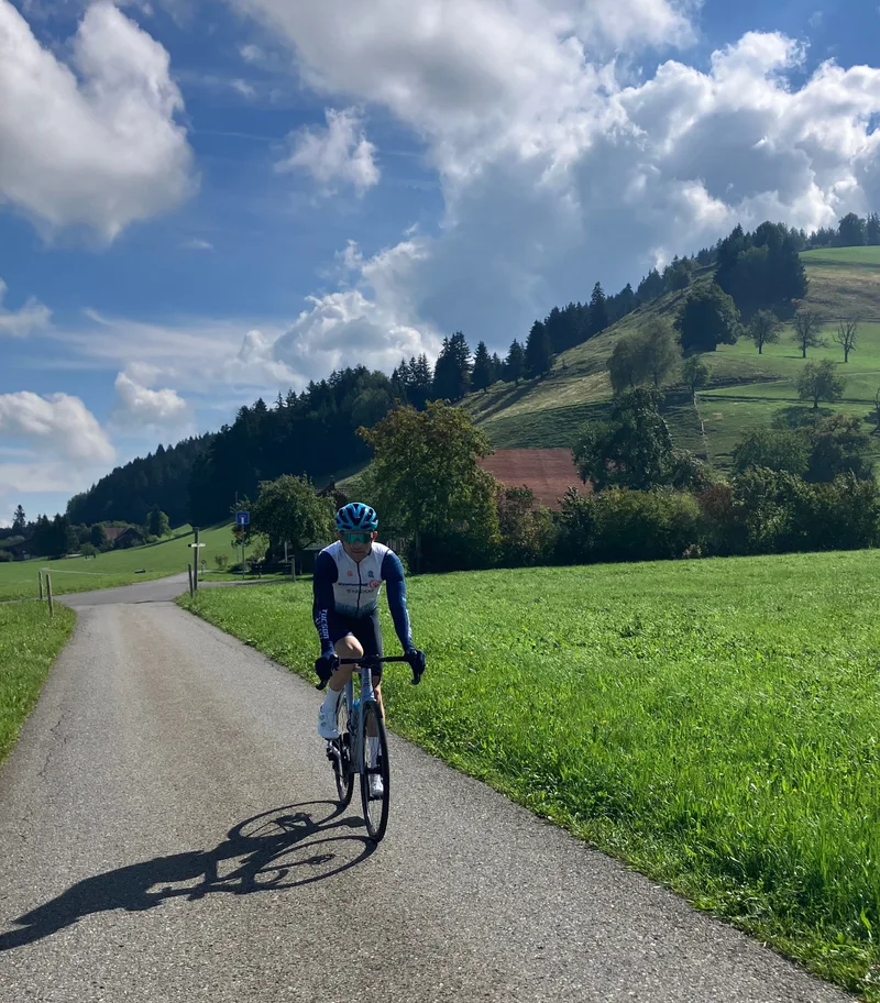Cyclist riding a quiet country lane through green meadows below the forested slopes of the Schindellegi